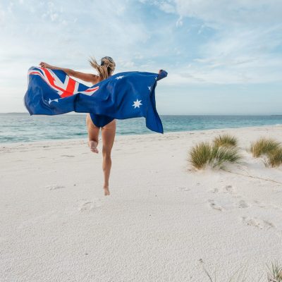 Jump for joy.  Woman leaping into the air with the Australian flag on a pretty beach.  Australian supporter, sports, fan, Australia Day celebrations